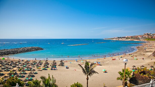 A beach with umbrellas, lounge chairs, and a rocky breakwater. - A revisar (Los Cristianos)