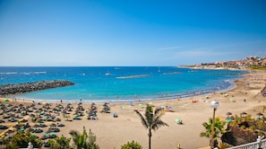 A beach with umbrellas, lounge chairs, and a rocky breakwater. - A revisar (Los Cristianos)