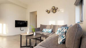 A modern living room with a sectional sofa, a small round table, and a flat-screen TV mounted on the wall.