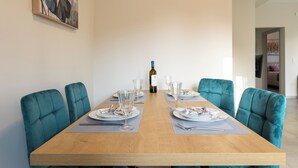 A dining table set with plates, glasses, and cutlery, flanked by teal upholstered chairs, with a bottle of wine on the table.
