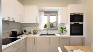A modern kitchen with a sink, stove, and oven, a dining table with a chair, and a window with a view of the outdoors.