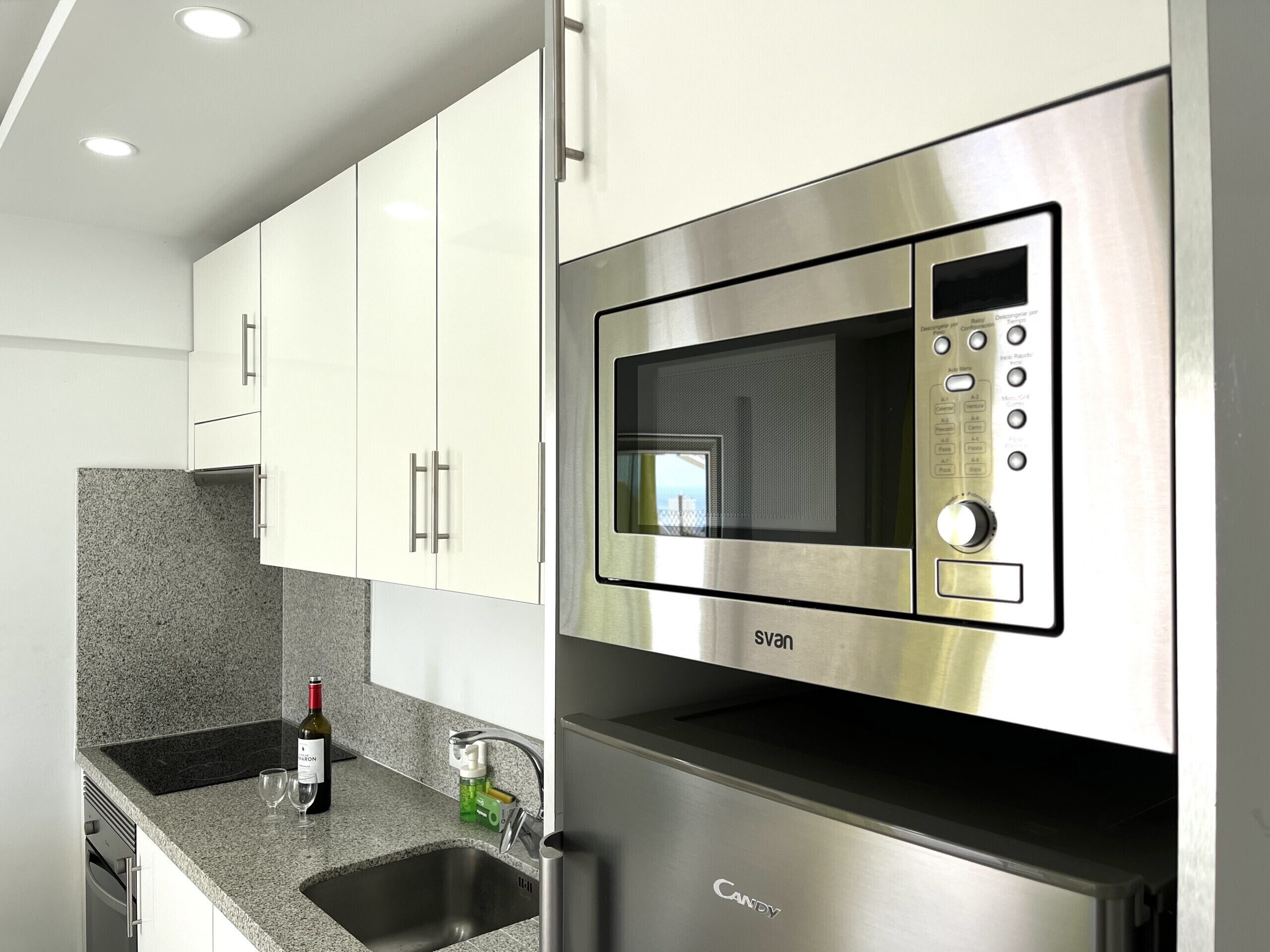 Una cocina moderna con gabinetes blancos, un microondas de acero inoxidable y un horno empotrado.