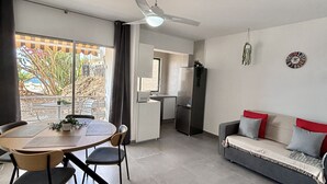 A modern living room with a dining area, a sofa, a ceiling fan, and a kitchen in the background. - Coastal Retreats Beach & Ocean View Playa Arena (Santiago del Teide)