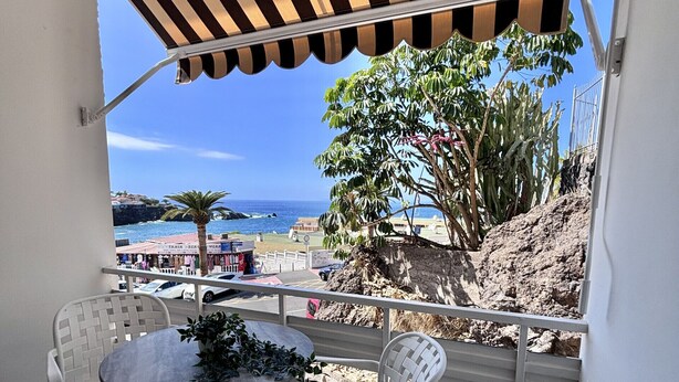 A balcony with white plastic chairs and a table, overlooking a rocky landscape and the sea. - Coastal Retreats Beach & Ocean View Playa Arena (Santiago del Teide)