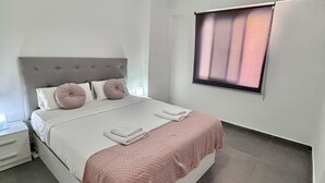 A modern bedroom with a bed, a ceiling fan, a window with blinds, and a bedside table. - Coastal Retreats Beach & Ocean View Playa Arena (Santiago del Teide)