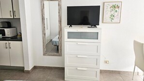 A small, modern room with a kitchenette, a flat-screen TV, a white cabinet with drawers, and a framed botanical illustration on the wall. - The Poolside Haven (Los Cristianos)