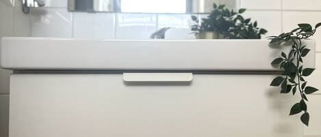 A white bathroom vanity with a mirror above it and a plant on the right side.