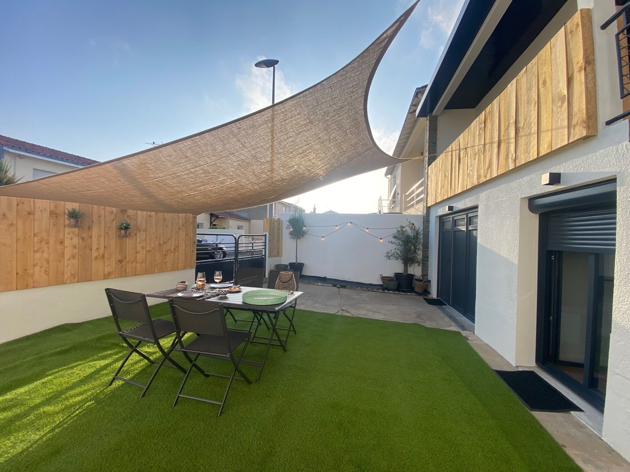 A patio with a table set for dining, surrounded by a wooden fence and a shade sail.