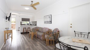 Un ambiente compatto con angolo cottura, divano, tavolo da pranzo e ventilatore a soffitto.