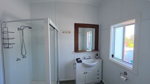 Un bagno con box doccia in vetro, specchio con cornice in legno, lavabo bianco con mobile contenitore e finestra vista su vegetazione.