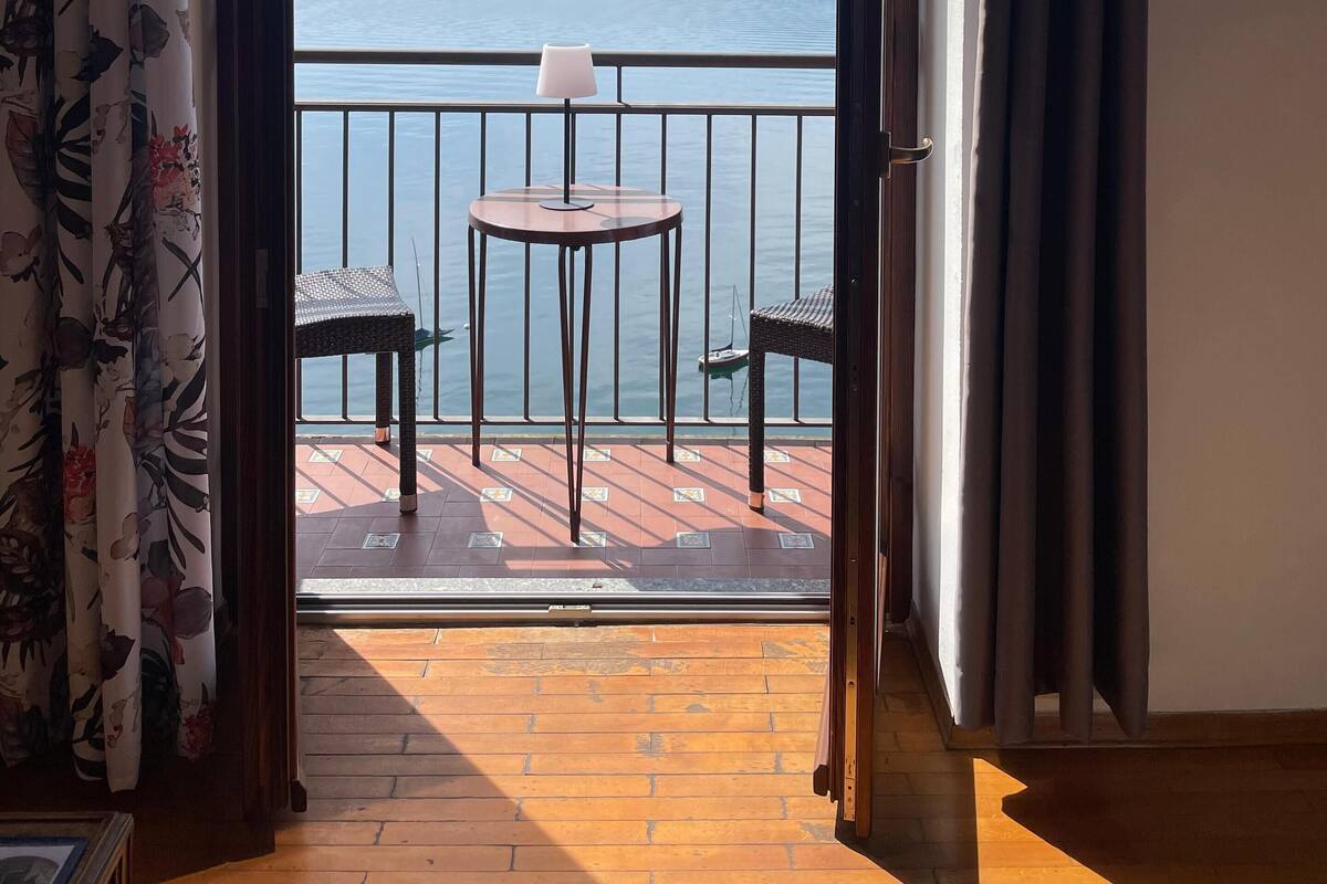 A balcony with a table and chairs, overlooking a body of water and distant mountains.