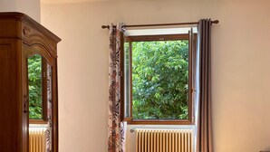 A room with a wooden floor, a bed with rolled towels, a radiator, and a window with curtains. - Villa Angelina (Cannero Riviera)