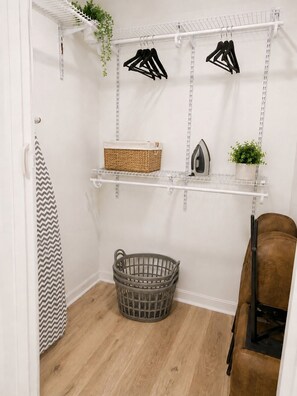 A laundry area with shelves, a basket, an iron, and a chair. - Comfortable, Peaceful Stay Near Tampa & Plant City (Seffner)