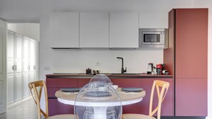 Una cocina moderna con armarios blancos, microondas y un comedor con una mesa redonda y dos sillas.