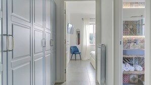Un pasillo con puertas blancas, una silla azul y un suelo de baldosas que conduce a un dormitorio con cama y un baño con azulejos decorativos.