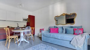 Una sala de estar moderna con un sofá azul, una mesa de comedor con sillas, una zona de cocina y un espejo grande en la pared.