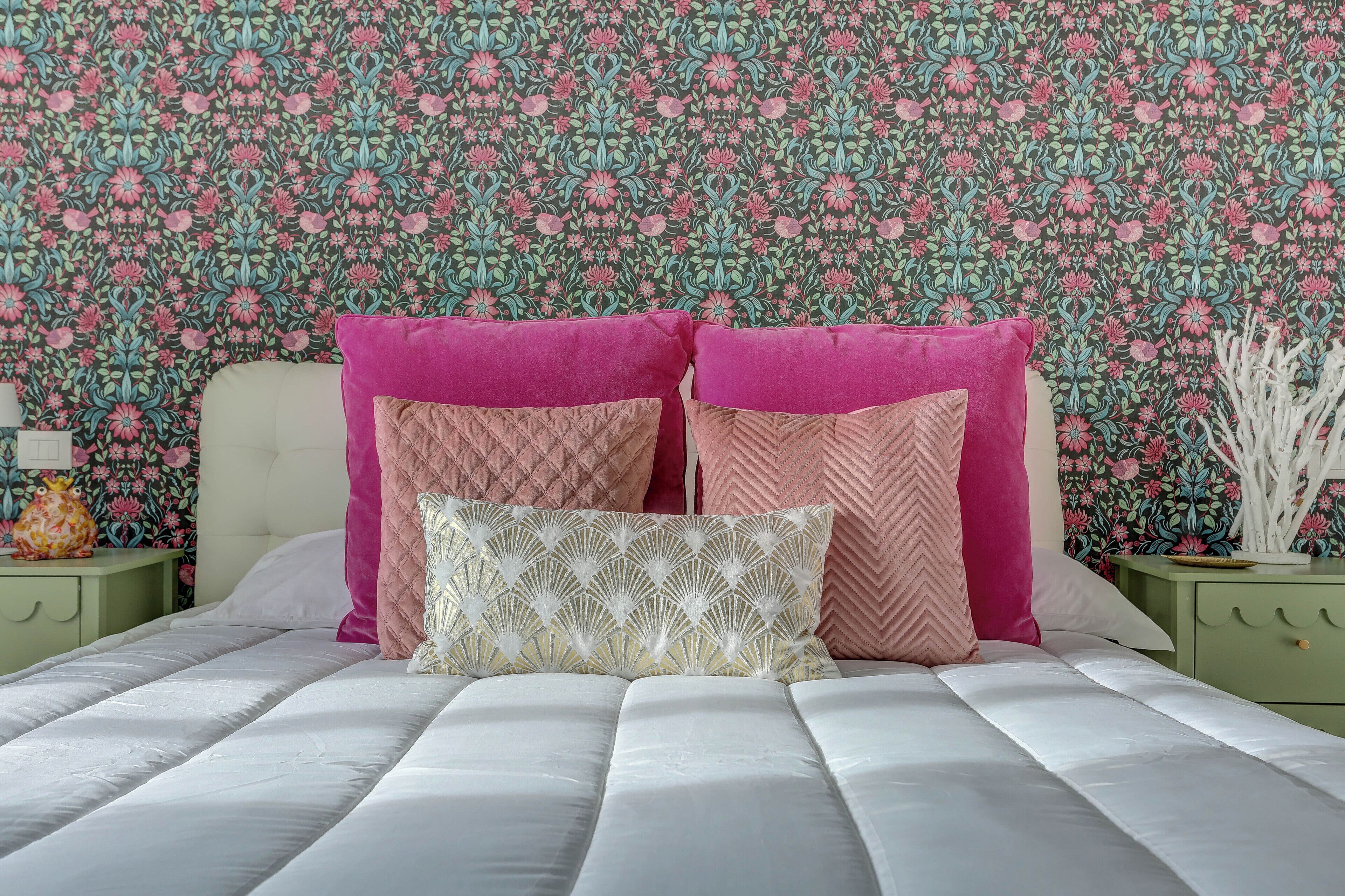 Een bed met een witte matras en roze kussens, voor een bloemen behang.
