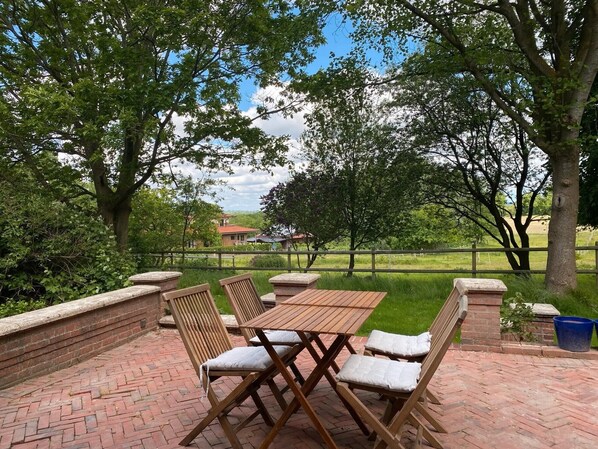 Eine Terrasse im Freien mit rotem Bodenbelag, einem Holztisch und Stühlen.