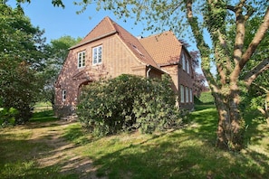 Ein Backsteinhaus mit Satteldach, umgeben von Bäumen und einer Rasenfläche.