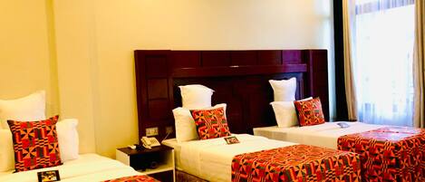 A hotel room with two single beds, a large wooden headboard, and a small bedside table with a phone.
