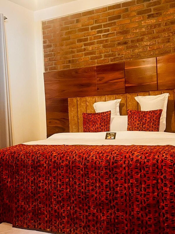 A hotel room with a brick-patterned headboard, white bedding, and a red patterned bedspread. - Sunset Retreat Hotel (Arusha)