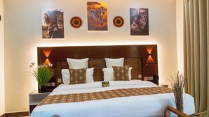 A hotel room with a large bed, a wooden headboard, and wall-mounted artwork depicting animals. - Sunset Retreat Hotel (Arusha)