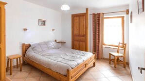 A bedroom with a wooden bed, a small bedside table, a chair, a window with curtains, and a door. - Gites Simond welcomes you to Arvieux in the heart of the Queyras Regional Park, (ARVIEUX)