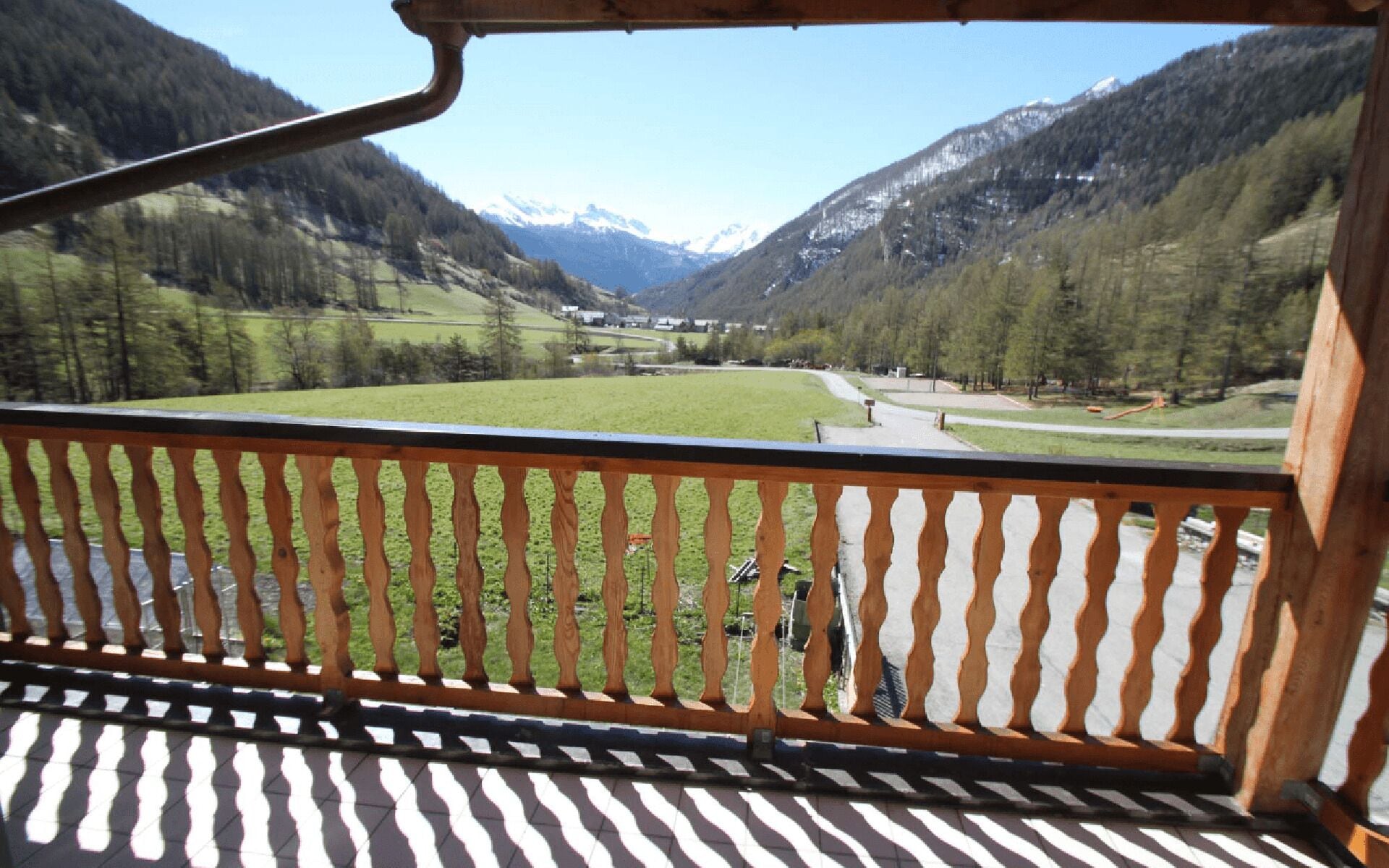 A balcony with a view of a valley, mountains, and a road.