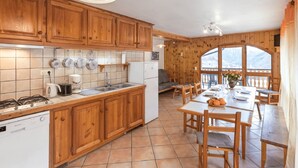 A kitchen with wooden cabinets, a stove, and a sink. There is a dining area with a table and chairs. - Gites Simond welcomes you to Arvieux in the heart of the Queyras Regional Park, (ARVIEUX)