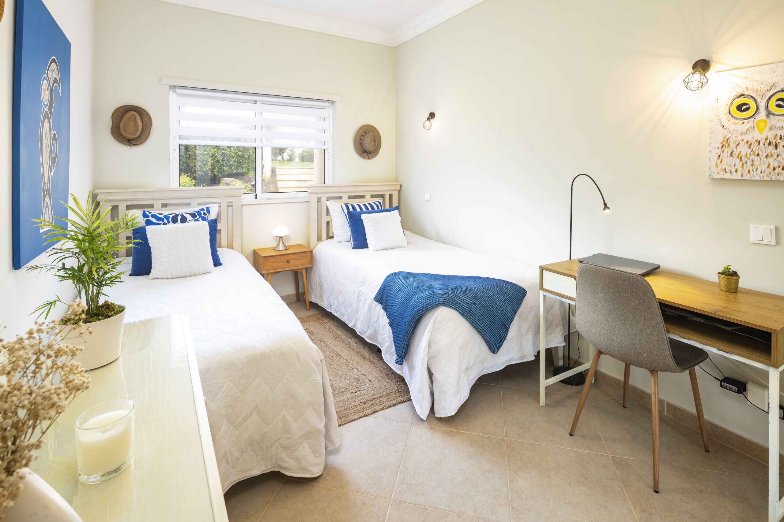 A bedroom with two beds, a desk, a chair, a window, and a wall art piece.