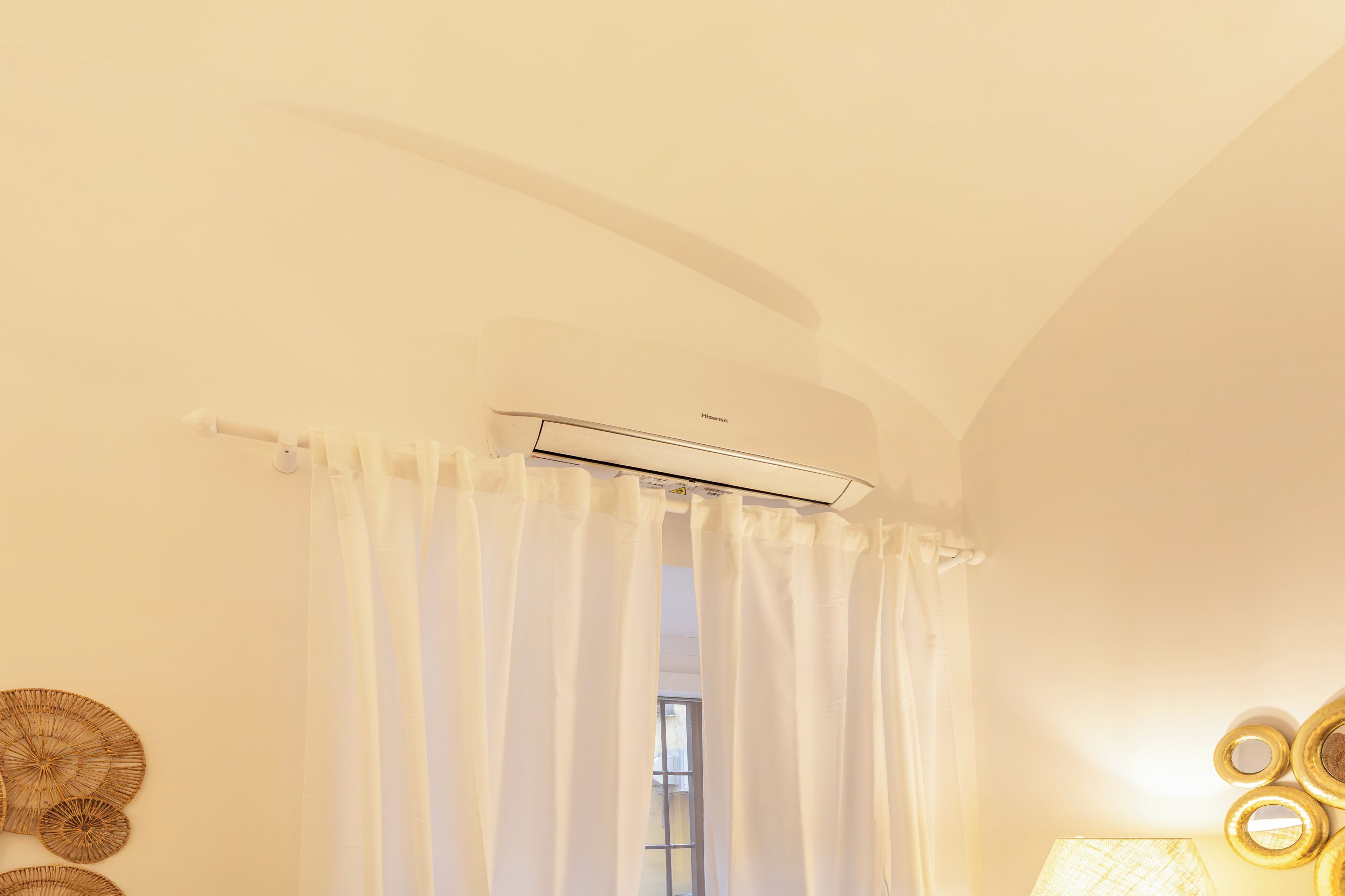 Una habitación con techo blanco, una ventana con cortinas blancas y un equipo de aire acondicionado instalado en la pared.