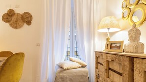 Ein Zimmer mit einer gepolsterten Bank, einem geschnitzten Holzschrank, einer Lampe und einer Buddha-Statue.