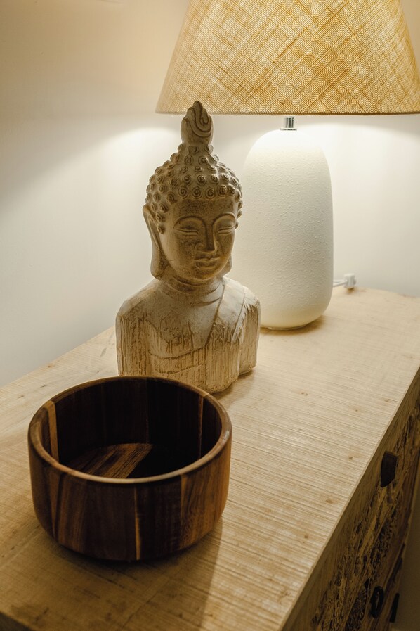 Une sculpture en bois représentant une tête de Bouddha, une lampe blanche et un bol en bois, le tout posé sur une table.