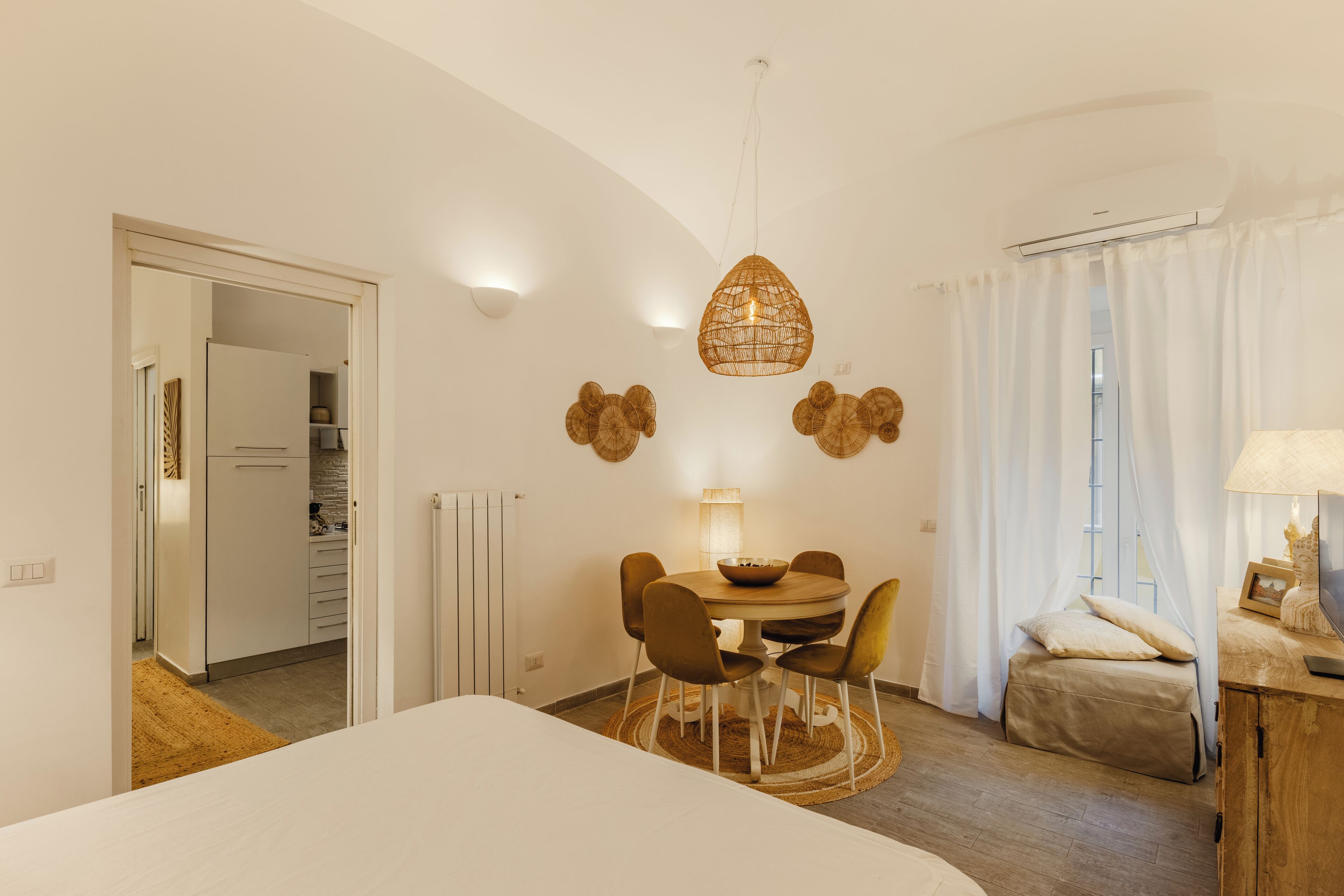 Ein modernes Schlafzimmer mit Bett, Esstisch mit Stühlen, einer Pendelleuchte und Blick ins Freie.