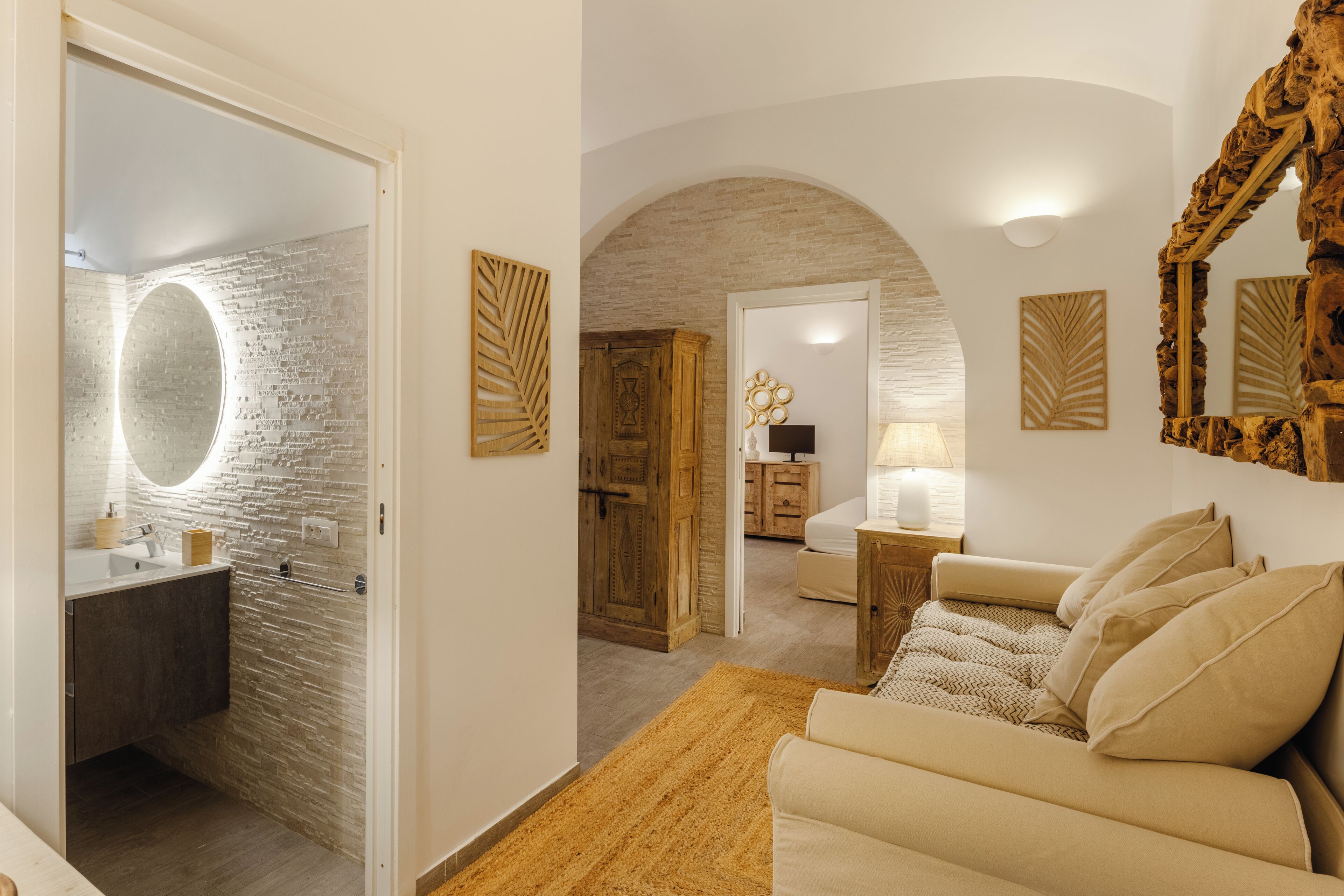 A modern interior with a stone wall, a round mirror, a wooden cabinet, a sofa, and a mirror with a rustic frame.