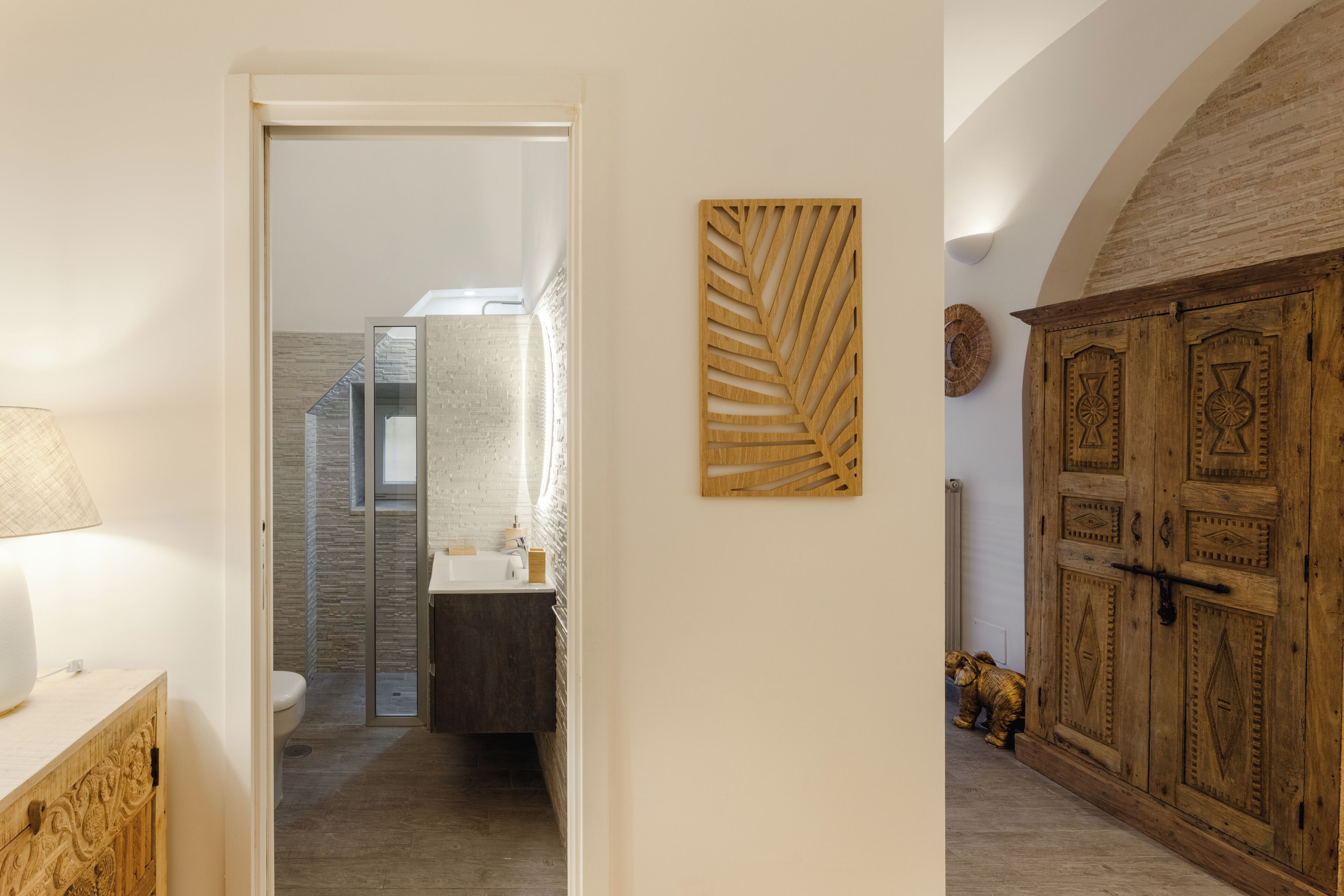 A hallway leading to a bathroom with a modern design, a wooden cabinet, and a decorative wall piece.