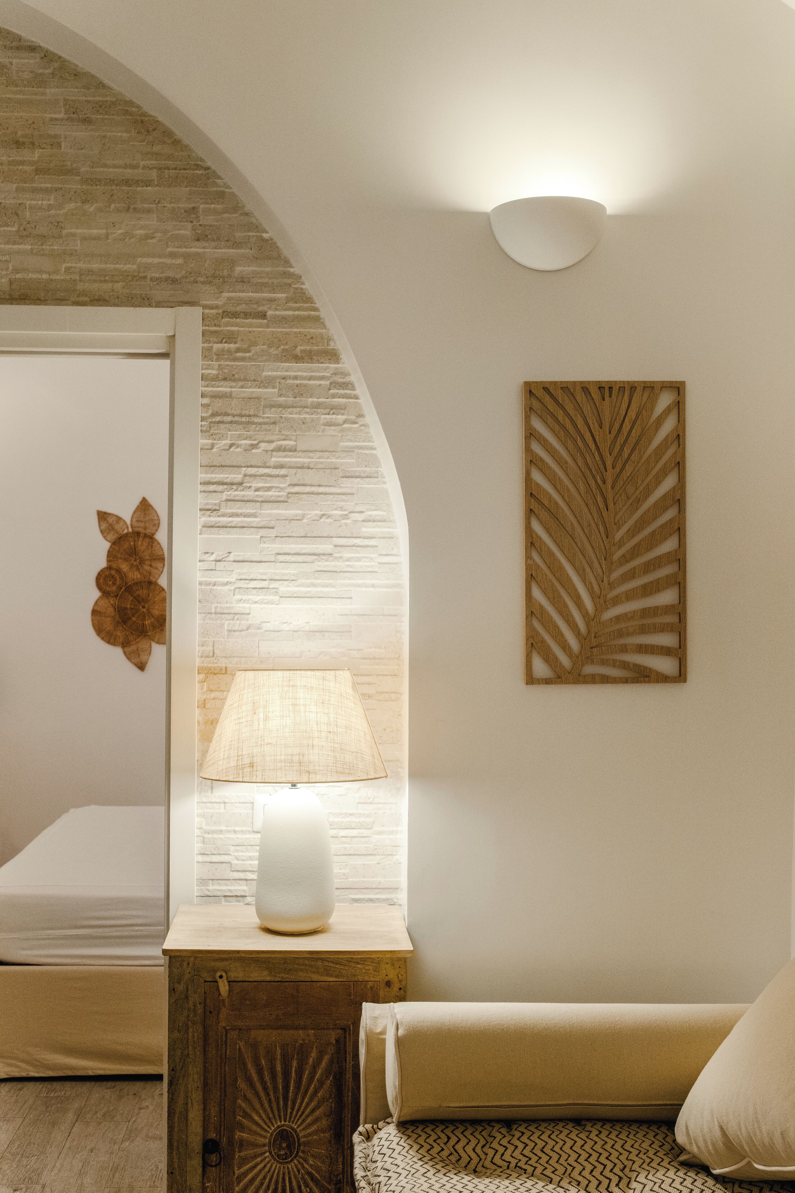 A bedroom with a bed, a bedside table with a lamp, a decorative wall piece, and a wooden cabinet.