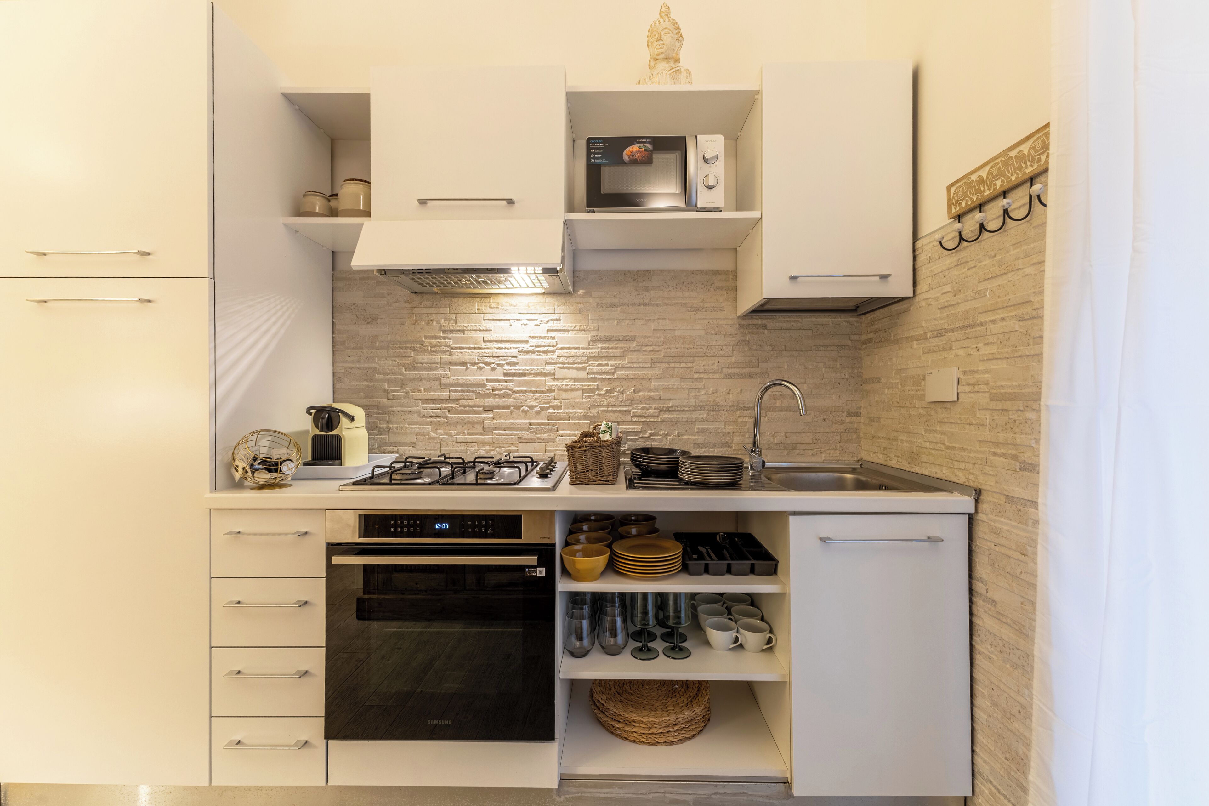 A compact kitchen with white cabinetry, a microwave, a gas stove, and a sink.