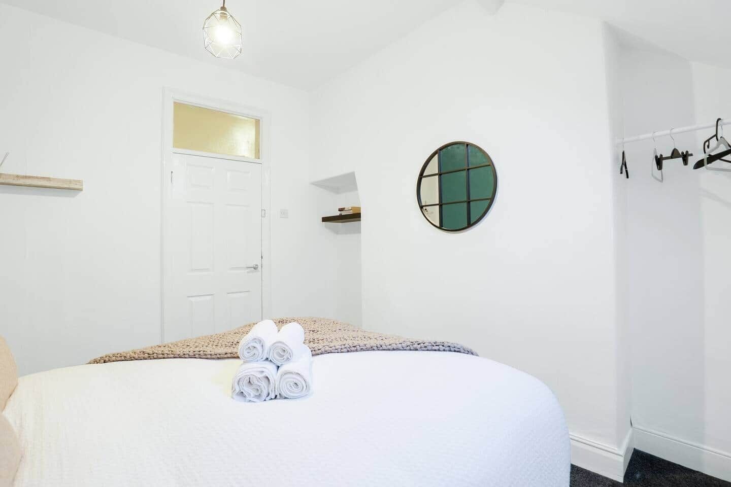 Un dormitorio con cama, un espejo redondo, una puerta y un perchero.