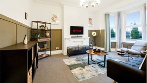 Ein Wohnzimmer mit Kamin, Wand-Fernseher, Bücherregal, Couchtisch und Sofa.