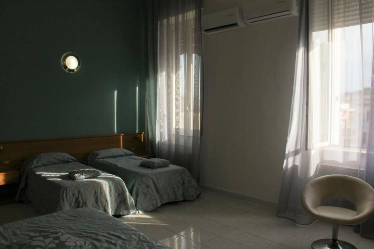 Una camera da letto con due letti, una sedia e una finestra con tende leggere.