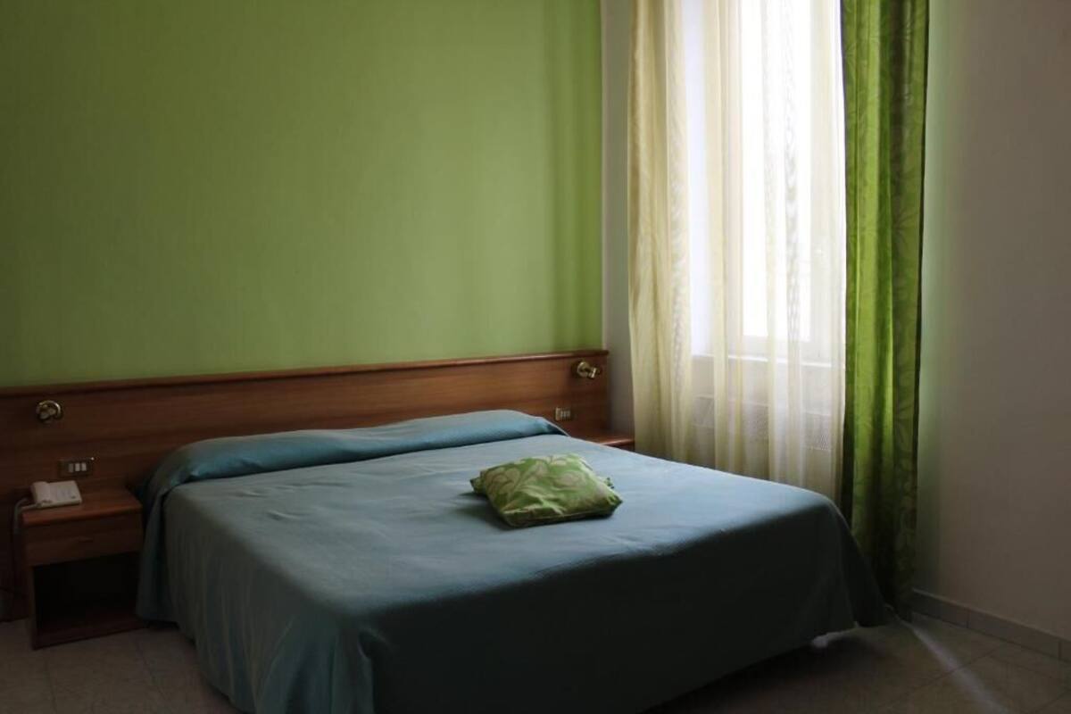 Un letto singolo con un cuscino verde in una stanza dalle pareti verdi e una testiera in legno.