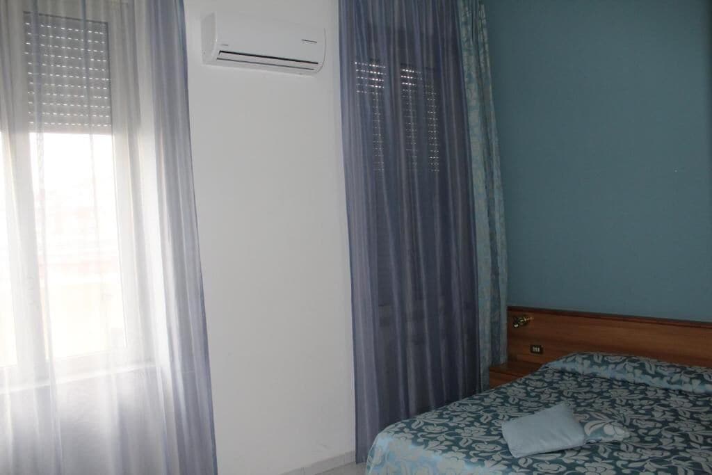 A bedroom with a bed, curtains, and an air conditioning unit.