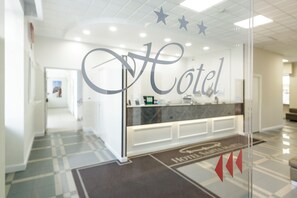 Ein Hotelrezeptionsbereich mit einer Glaswand, die das Wort 'Hotel' zeigt, und einem Empfangstresen.