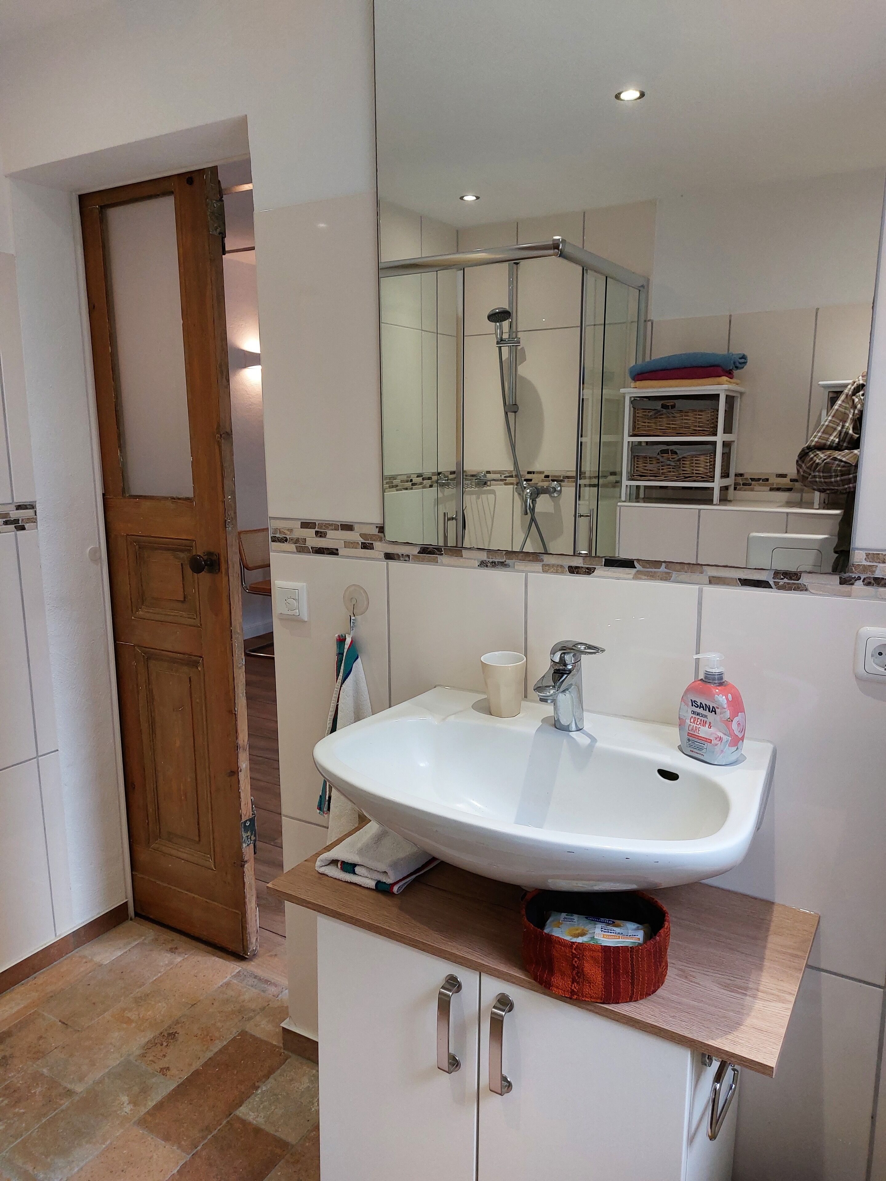 A bathroom with a white sink, a mirror, a shower, and a wooden door.