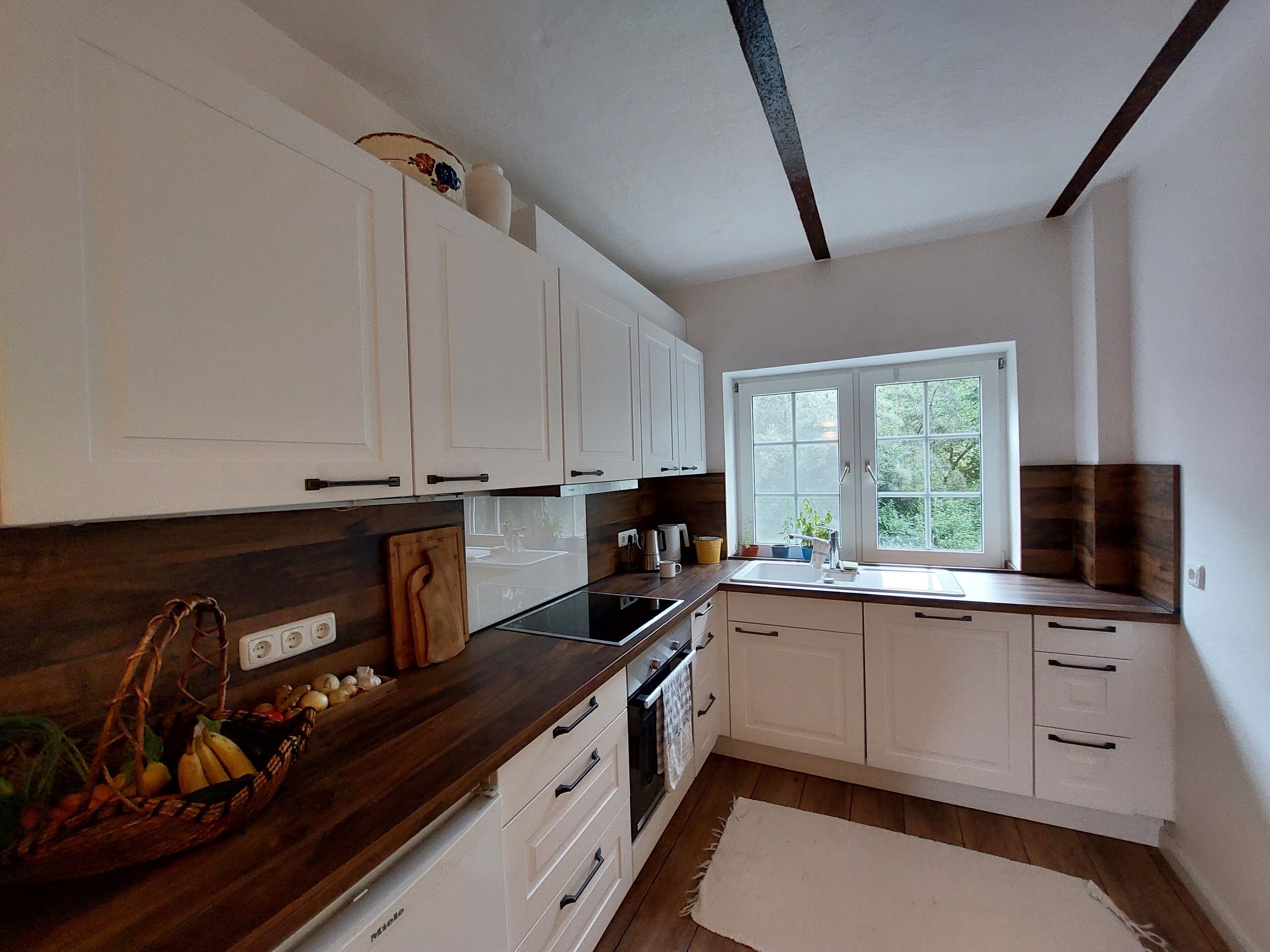 A modern kitchen with white cabinets, a wooden countertop, and a window providing natural light.