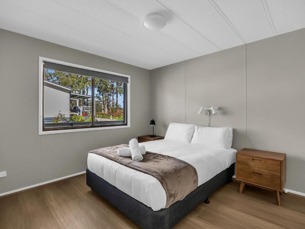 A modern bedroom with a large window, a bed, a bedside table, and a nightstand.