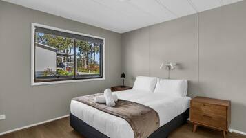 Un dormitorio moderno con un ventanal grande, una cama, una mesita de noche y una mesilla.