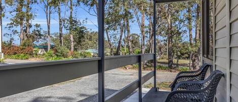Un espacio al aire libre cubierto con una terraza de madera, barandilla metálica y dos sillas de metal negro.