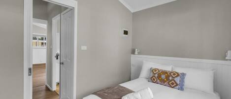 A bedroom with a bed, a door leading to another room, and a small window.